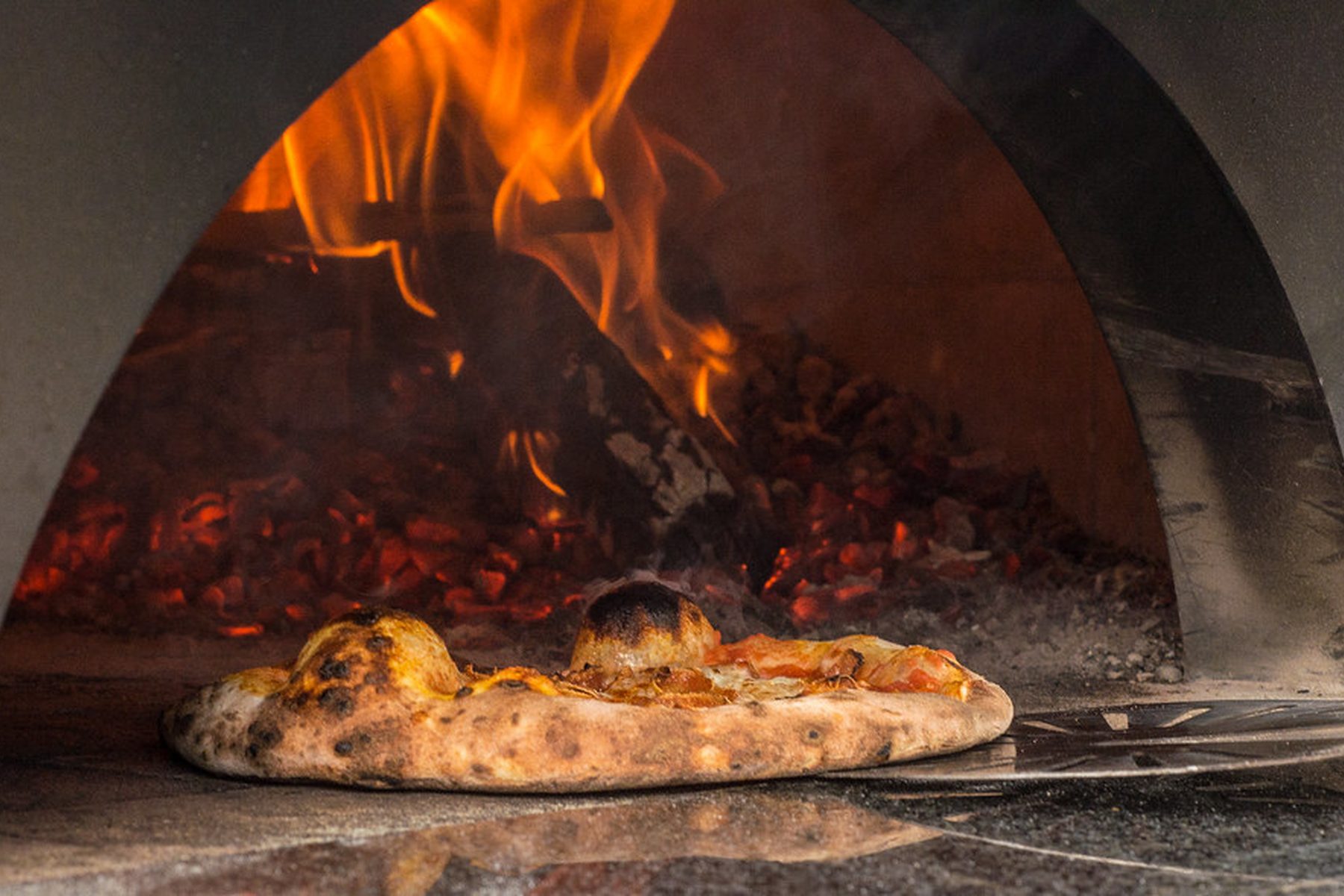 Pizza appena sfornata davanti alla bocca del forno acceso
